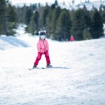 Little girl in pink ski costume skiing in downhill slope. Winter sport recreational activity