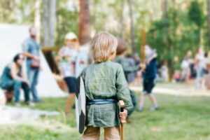 Viking game for kids. Rear view of little boy in medieval clothes holding wooden toy shield